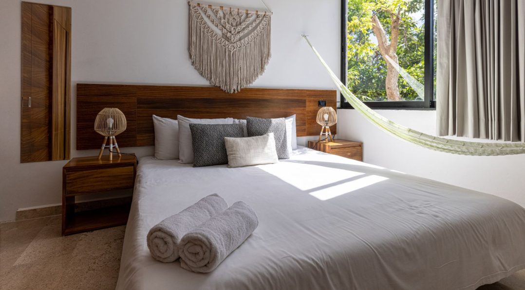 A cozy hotel room with sand-colored walls, white linens, and wooden accents, creating a warm and inviting atmosphere.